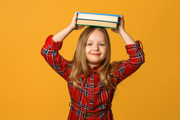 Portrait of a little girl schoolgirl on a yellow background. The child holds books on his head. The concept of education and school.