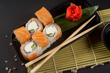 Close up sushi rolls in a black plate on dark background