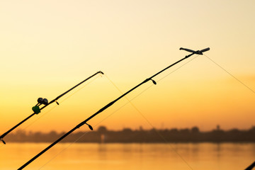 Silhouette of fishing poles under dramatic sunset and beautiful river.