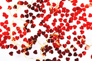 White background with red heart shaped confetti and string lights. Festive and holiday. St. Valentine's day concept. top view, flat lay