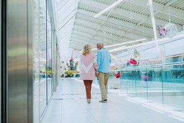 Cute senior couple holding hands and walking in the mall. Backs turned.