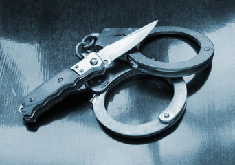 Steel metallic handcuffs and knife on wooden table