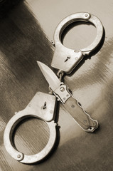 Steel metallic handcuffs and knife on wooden table