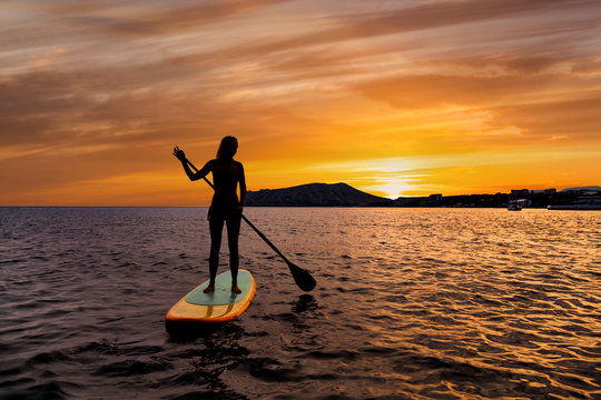 Stand up paddle boarding on a quiet sea with warm summer sunset colors.