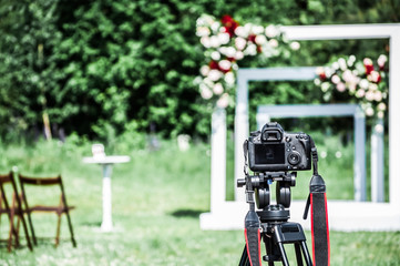 A photo camera mounted on a tripod is ready to shoot a festive wedding ceremony.