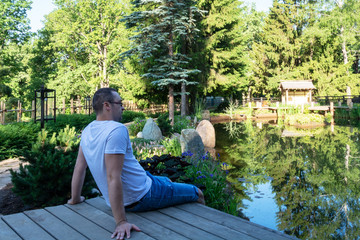 Fototapeta premium Young attractive man meets a dawn while sitting on a wooden pier in front of a small pond