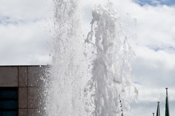 splash of water from the fountain against cloudy sky and modern building in background 