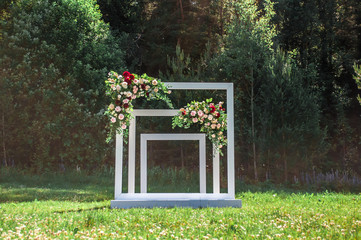 Wedding arch decorated with flowers in the open air. A beautiful wedding is set up. Wedding ceremony on the green lawn in the garden. Part of the festive decor, flower arrangement.