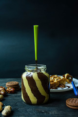 Chocolate spread or nougat cream with hazelnuts in a glass jar on a dark wooden background.