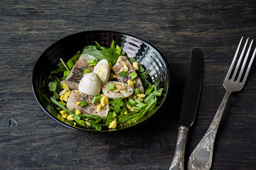 Marinated herring with arugula, onions, boiled quail eggs and lemon juice and olive oil. Delicious salad. Proper nutrition. Dark wooden background.