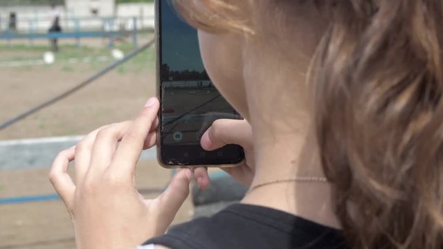 Young caucasian girl holding mobile phone in equestrian center and taking picture with phone of equestrian