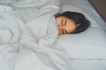 Woman stretching in bed after waking up, back view. Woman sitting near the big white window while stretching on bed after waking up with sunrise at morning, back view.