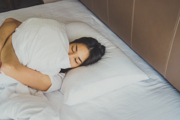 Woman stretching in bed after waking up, back view. Woman sitting near the big white window while stretching on bed after waking up with sunrise at morning, back view.