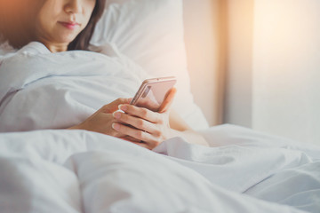 Asian Girl in bed room on the bed with the mobile phone.Closeup portrait of young sleepy exhausted woman lying in bed using smartphone,
