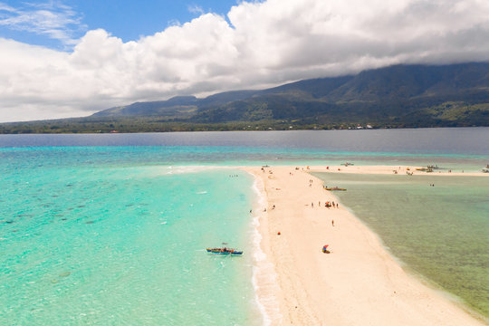 white beach overlooked by volcanos on camiguin island near mindanao in the philippines. Tourists rest on the white sandy island, view from above.