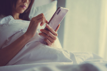 Asian Girl in bed room on the bed with the mobile phone.Closeup portrait of young sleepy exhausted woman lying in bed using smartphone,