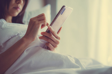 Asian Girl in bed room on the bed with the mobile phone.Closeup portrait of young sleepy exhausted woman lying in bed using smartphone,