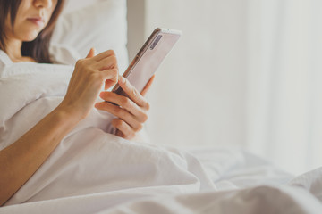 Asian Girl in bed room on the bed with the mobile phone.Closeup portrait of young sleepy exhausted woman lying in bed using smartphone,
