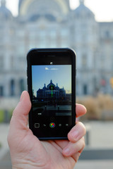 Detail view of a person's hand holding a smartphone device taking up photos of a monument cathedral
