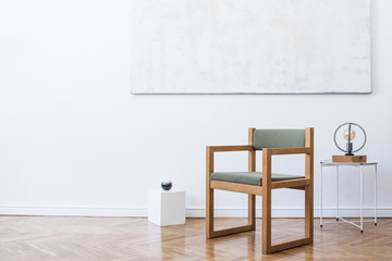 Minimalistic and modern interior of open space with design green armchair, triangle geometric sculpture , stylish lamp and elegant accessories. Abstract paintings on the white wall. Template.