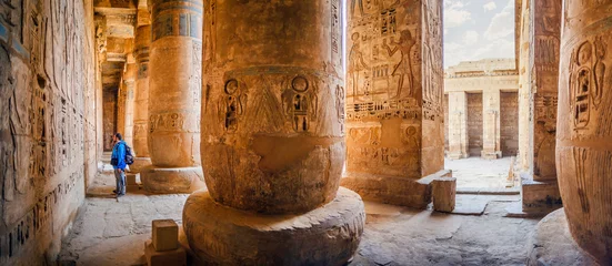 Foto op Plexiglas De toerist beschouwt de hiërogliefen op de muren van de tempel van Medinet Habu. Egypte, Luxor. De dodentempel van Ramses III in Medinet Habu is een belangrijke structuur uit de periode van het Nieuwe Rijk © Konstantin