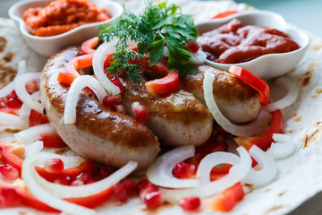 Fried pork sausages on pita bread with ketchup and Armenian appetizer Aivar with vegetables. Lavash, red bell pepper, onions, sausages. Oktoberfest food, the concept of the pub
