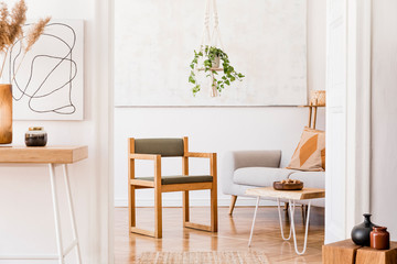 The nice boho open space interior at cozy apartment with design gray sofa, wooden desk, armchair and coffee table, plants and elegant accessories. Mock up poster on the white wall. Stylish home decor.