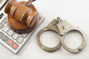Wooden gavel, calculator and handcuffs on white table. financial fraud concept