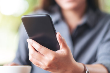 Closeup image of a woman holding  and using mobile phone with coffee cup on wooden table in cafe