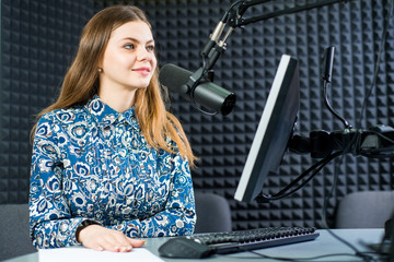 Young pretty woman radio presenter sitting in studio with headphones and talking on the air