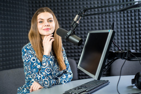Young pretty woman radio presenter sitting in studio with headphones and talking on the air