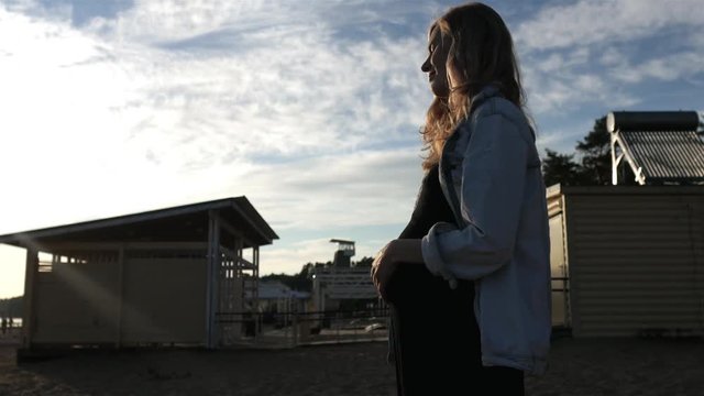 pregnant girl is standing at sunset on the beach
