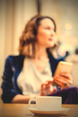 cup of tea on the table and a woman with a smartphone in the blur zone