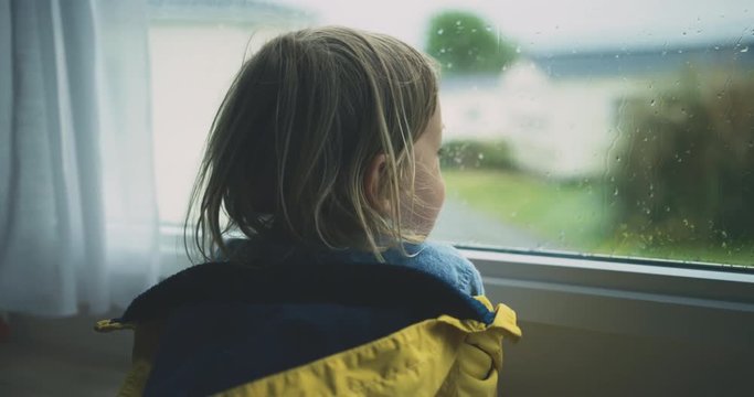Little toddler watching the rain from inside a caravan