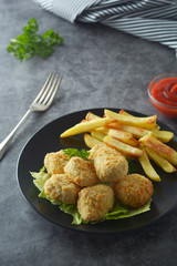 Chicken nuggets with french fries on dark background, top view.