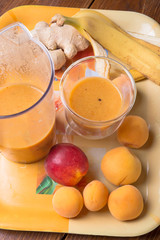 fresh fruit smoothie with banana and apricots at orange  tray  at wooden table