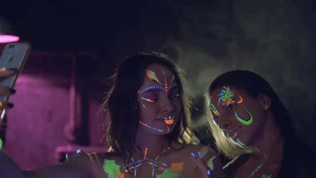 Two woman maiking selfie with smartphone at neon party