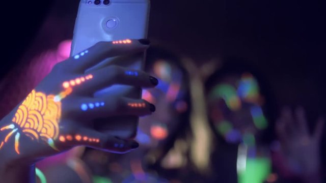 Two woman maiking selfie with smartphone at neon party