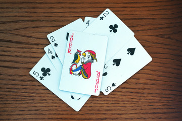 cards of two, three, four and five of peak and cross color on table, on top of them is joker symbol of good luck and winnings