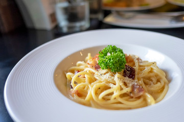 Pasta carbonara or spaghetti with ham, parsley, bacon, parmesan cheese in white dish.