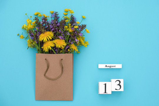 Wooden cubes calendar August 13 and field colorful rustic flowers in craft package on blue background. Greeting card Flat Lay Concept Hello August Template with copy space for text and design