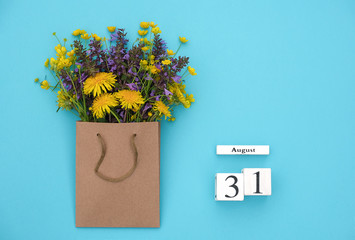 Wooden cubes calendar August 31 and field colorful rustic flowers in craft package on blue background. Greeting card Flat Lay Concept goodbye summer Template with copy space for text and design