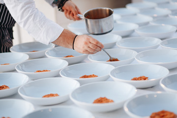 Young chef cook putting tomato sauce on dishes