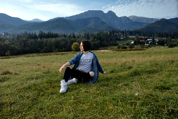 Fototapeta na wymiar Girl sitting on grass. Mountains as a background