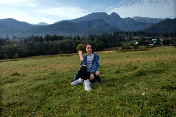 Fototapeta premium Girl sitting on grass. Mountains as a background