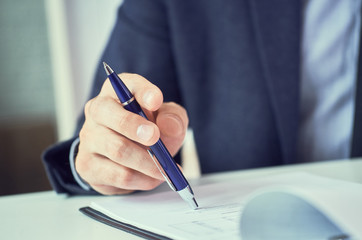 Businessman reading rental contract before making a deal. Corporate man with pen in hand working in modern office, signing business document on desk. close up.