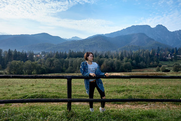 Girl sitting on wooden fence. Mountains as a background