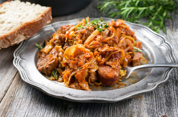 Traditional Polish kraut stew bigos with sausage, meat and mushrooms as closeup on a pewter plate on an old wooden table 