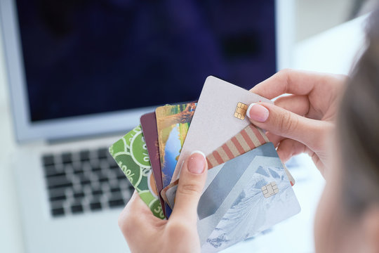 Woman hand holding various credit cards in order to make a purchase in the online store using a laptop.