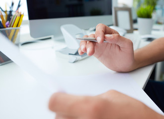 Young businessman reading legal documents at office, family considering mortgage loan or insurance, studying contract details, terms and conditions. Close up view of hands holding papers.